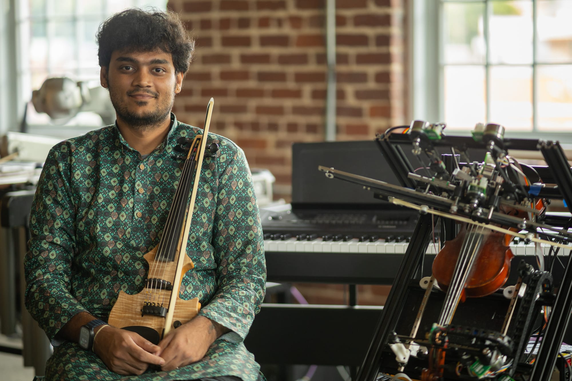 Seated with a violin in the lab, a violin-playing robot beside him