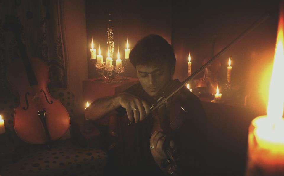 Playing the violin by candlelight, a cello resting in the shadows behind