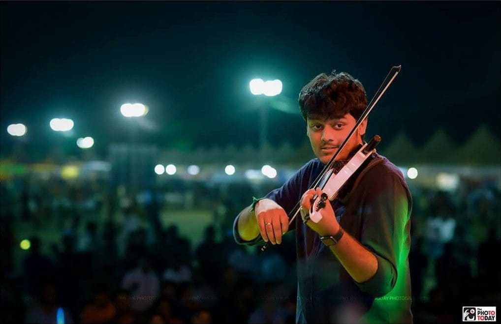 Performing on electric violin at a night-time open-air concert in front of a large crowd