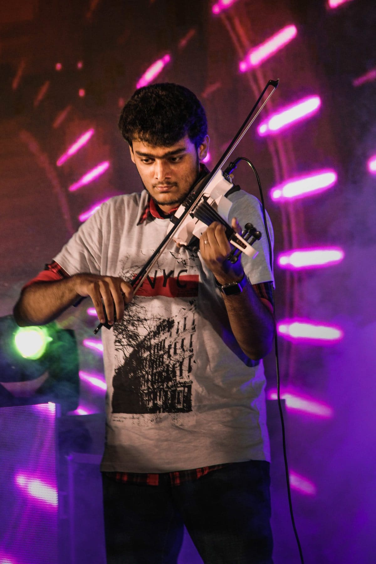 Playing a white electric violin on stage, framed by pink and violet stage lights