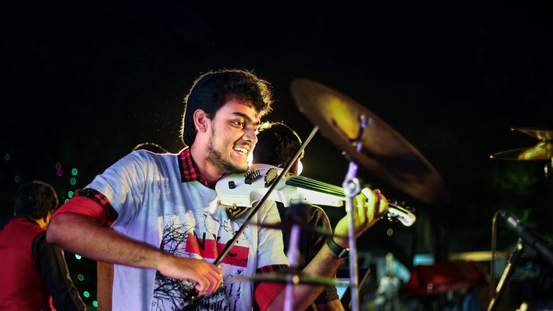 Performing on electric violin on a festival stage at night, cymbals behind him