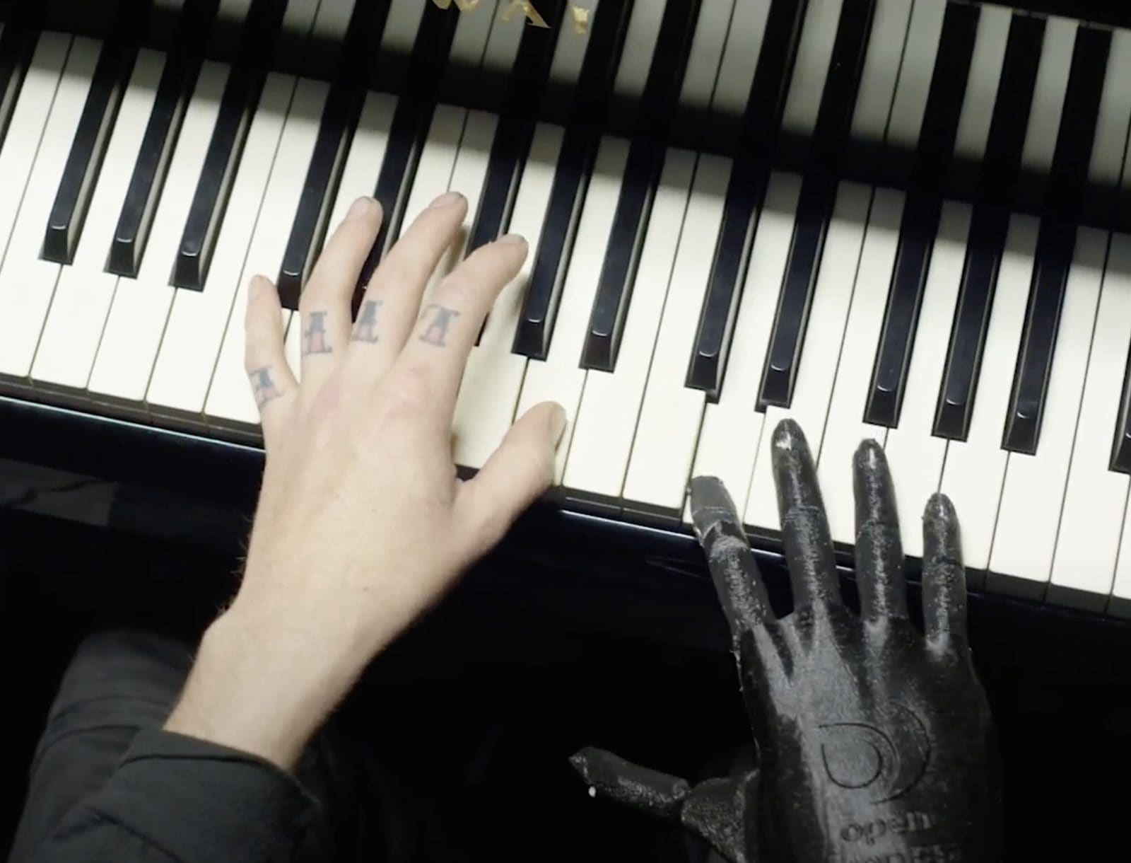 A human hand and a dark prosthetic hand side by side on a piano keyboard